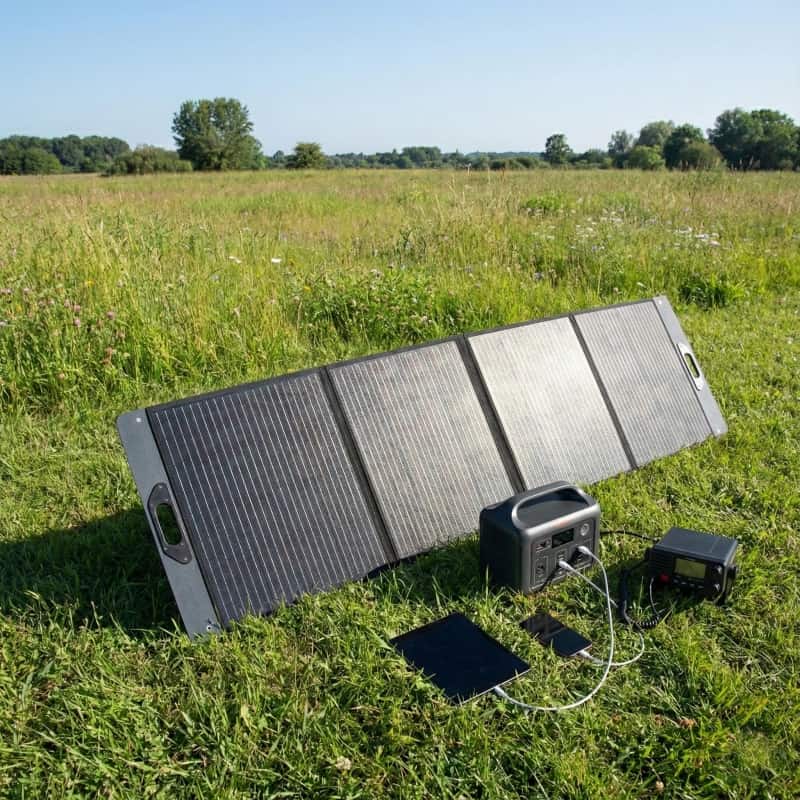 Portable 200W solar panel set up on grass, angled towards the sun to charge a portable generator for camping.