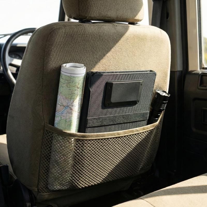 A compact, folded 45W solar panel stored neatly in the mesh seat-back pocket of a rugged 4WD vehicle, alongside a map and flashlight for emergency backup.